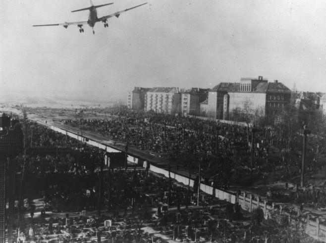 A four-engine aircraft on low approach over rubble and apartment blocks in Berlin