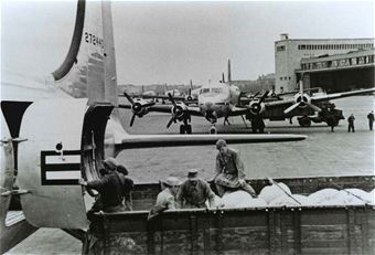 Ground crews unloading sacks from transports parked in front of an airport terminal